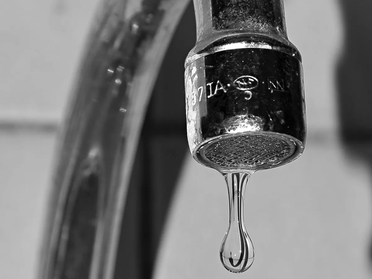 Chrome faucet with a single drop of water falling from the spout