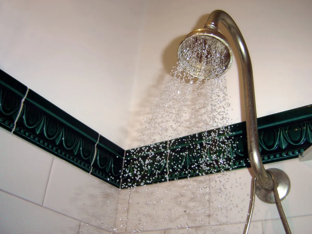 Wall-mounted shower head spraying water above a dark tile border