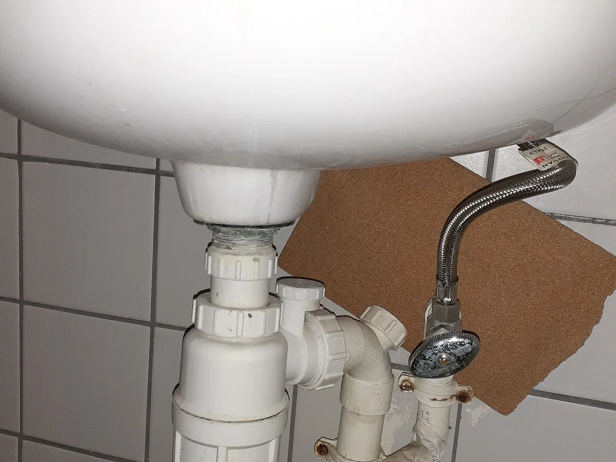 Exposed drain pipes and trap under a wall-mounted hand sink